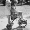 Girl & Her Sister Riding Tricycle Poster Print - 18 x 24 in.